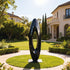 Large Abstract Black Oval Stainless Steel Sculpture in a garden with a house in the background