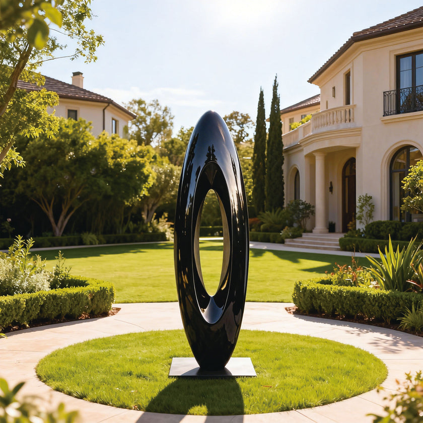 Large Abstract Black Oval Stainless Steel Sculpture in a garden with a house in the background