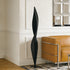 Abstract Slender Twisting Leaf Stainless Steel Sculpture and a brown leather sofa.