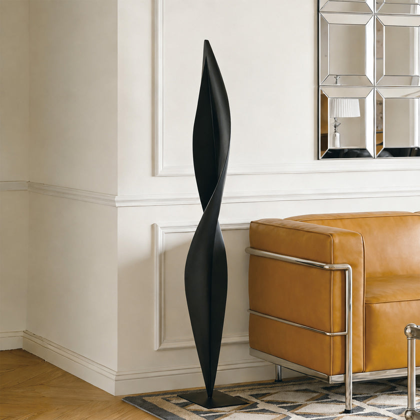 Abstract Slender Twisting Leaf Stainless Steel Sculpture and a brown leather sofa.