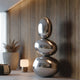 Large Mirror Polished Stainless Steel Sculpture Asymmetrical Spheres, lamp, and plant against a wooden wall.