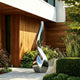 Abstract Silver Vessel Stainless Steel Sculpture in a garden setting with a wooden wall and plants.