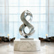 Fluid Infinity Loop Stainless Steel Sculpture on a marble base in a room with large windows