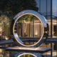 Modern Stainless Steel Lighting Sculpture Glowing Loop with illuminated interior reflecting a building and trees at night.