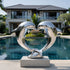 Romantic Heart Shaped Leaping Dolphins Stainless Steel Sculptures by a poolside in front of a luxury villa