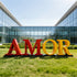 Iconic Pop Art AMOR Contemporary Art Sculpture in red and yellow, placed on a green lawn in front of a modern glass building.