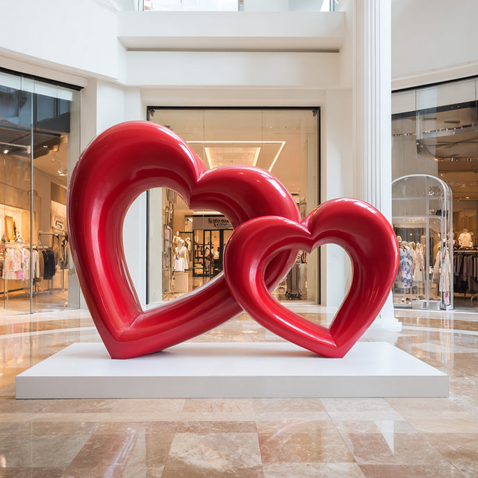 Interlocking Double Hearts Modern Abstract Sculpture Large Indoor Statues on a white rectangular pedestal in a modern indoor shopping mall atrium.