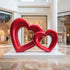 Interlocking Double Hearts Modern Abstract Sculpture Large Indoor Statues on a white rectangular pedestal in a modern indoor shopping mall atrium.