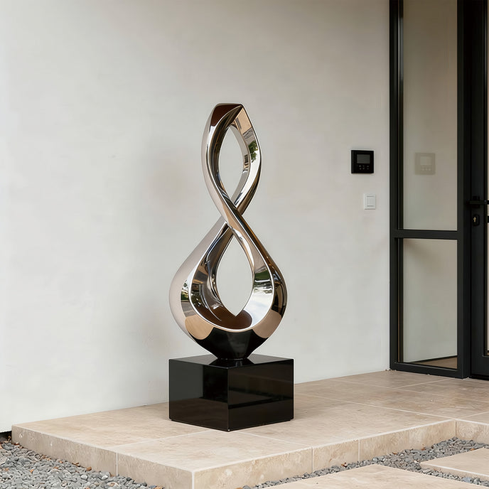 Gleaming Infinity Abstract Stainless Steel Sculpture on a glossy black rectangular base, displayed on a stone terrace in front of a minimalist building.