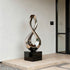 Gleaming Infinity Abstract Stainless Steel Sculpture on a glossy black rectangular base, displayed on a stone terrace in front of a minimalist building.
