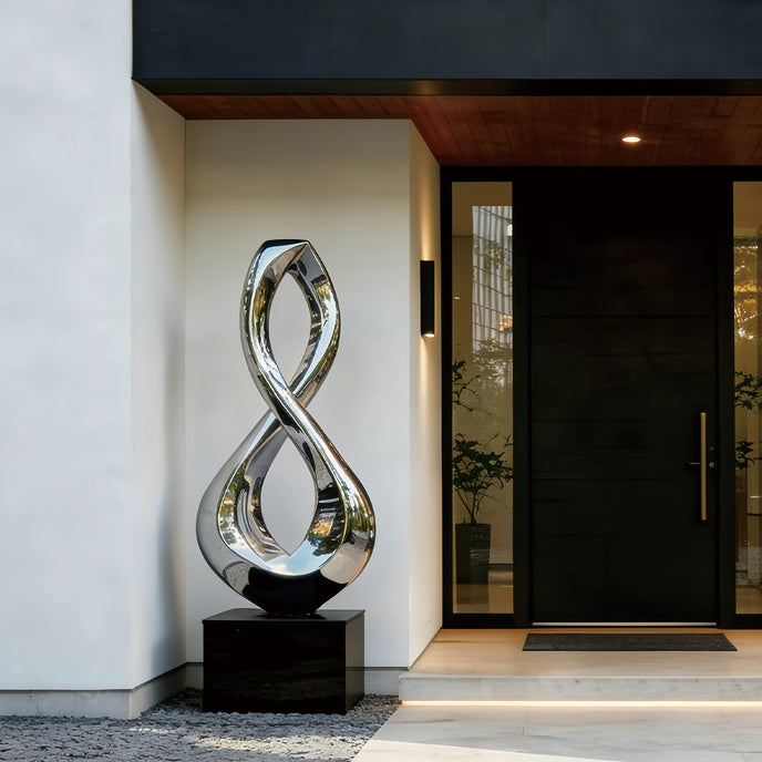 Gleaming Infinity Abstract Stainless Steel Sculpture on a black rectangular pedestal in front of a contemporary building entrance with a black door and white wall.