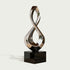 Gleaming Infinity Abstract Stainless Steel Sculpture on a glossy black rectangular base, set against a light gray background.