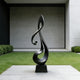 Lyrical Musical Note Black Stainless Steel Sculpture on a rectangular black base, set outdoors on a light stone patio with green grass and a minimalist concrete building in the background.