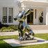 A large, glossy adorable Cartoon Puppy Outdoor Stainless Steel Sculpture on a rectangular base, placed outdoors on a lawn in front of a white house with steps and windows.