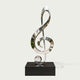 Modern Musical Note Outdoor Stainless Steel Sculpture on a rectangular black base, photographed against a plain light warm-gray background.