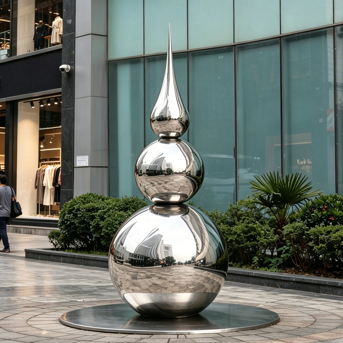 Striking Teardrop Tower Outdoor Stainless Steel Sculpture with a stacked spherical and teardrop silhouette stands on a circular base in an outdoor plaza in front of a modern glass building.
