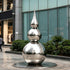 Striking Teardrop Tower Outdoor Stainless Steel Sculpture with a stacked spherical and teardrop silhouette stands on a circular base in an outdoor plaza in front of a modern glass building.