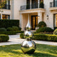 Striking Teardrop Tower Outdoor Stainless Steel Sculpture stands on a manicured lawn in front of a grand residential house with trimmed hedges and a stone walkway.