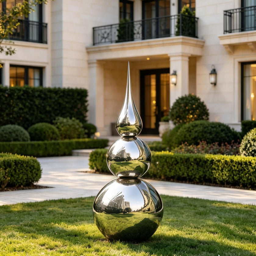 Striking Teardrop Tower Outdoor Stainless Steel Sculpture stands on a manicured lawn in front of a grand residential house with trimmed hedges and a stone walkway.