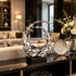 Dynamic Splashing Wave Mirror Stainless Steel Sculpture Large Outdoor Statuary on a black rectangular base, displayed on a dark console table in a modern, upscale living room setting next to a floral arrangement and decorative plate.