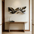 Polished stainless steel wall sculpture with flowing ribbon-like curves and reflective surfaces, displayed above a console table in a modern luxury interior.