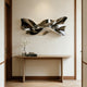 Polished stainless steel wall sculpture with flowing ribbon-like curves and reflective surfaces, displayed above a console table in a modern luxury interior.