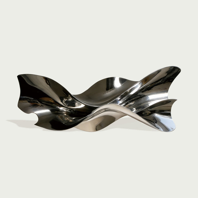 Polished stainless steel wall sculpture with flowing ribbon-like curves and reflective surfaces, displayed above a console table in a modern luxury interior.