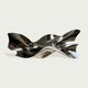 Polished stainless steel wall sculpture with flowing ribbon-like curves and reflective surfaces, displayed above a console table in a modern luxury interior.
