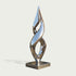 A modern abstract metallic sculpture with a reflective silver finish, mounted on a square base against a light gray background.