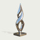 A modern abstract metallic sculpture with a reflective silver finish, mounted on a square base against a light gray background.