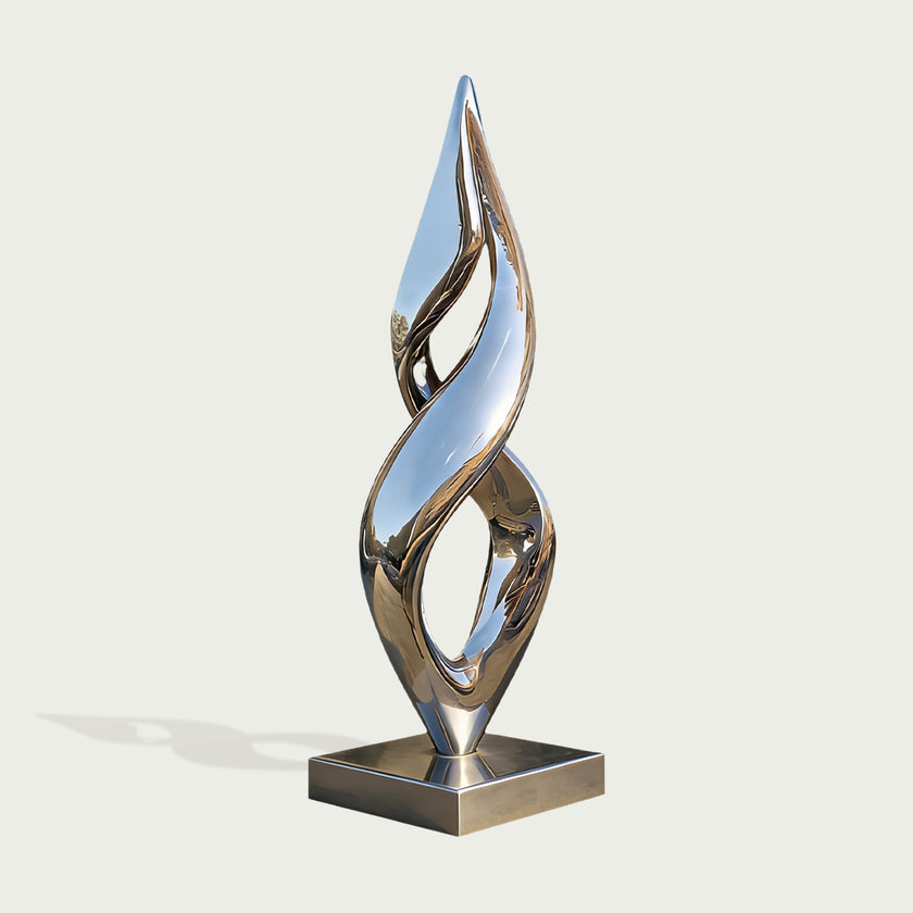 A modern abstract metallic sculpture with a reflective silver finish, mounted on a square base against a light gray background.