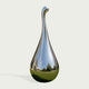 A polished chrome teardrop-shaped sculpture with a reflective neck, shown on a light gray background. The mirror-like surface reflects a blue sky, trees, and green grass.