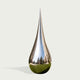 A teardrop-shaped reflective sculpture made of highly polished metallic silver, featuring a mirrored surface that reflects a park scene and a green grassy base, set against a solid off-white background.