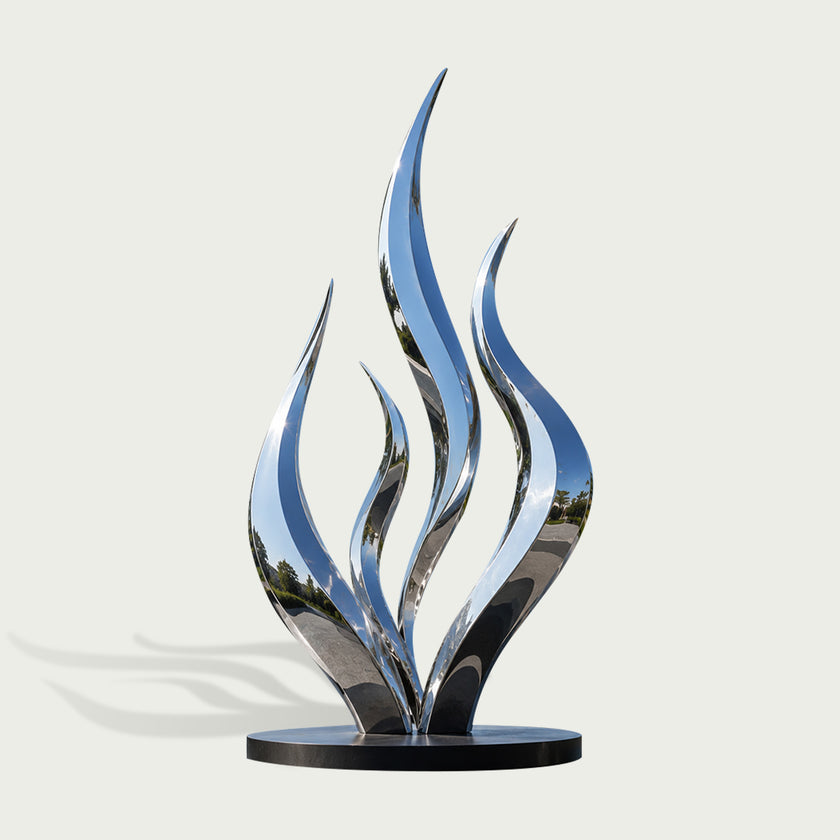 A modern abstract flame-shaped sculpture made of highly polished reflective metal, mounted on a round black base against a light gray background.