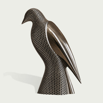A modern metallic bird sculpture with a perforated honeycomb pattern on its body and a smooth, reflective wing, displayed on a light off-white background.