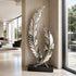 A mirror-polished stainless steel sculpture of two intersecting curved feathers on a black base. Displayed in a luxury hallway, this reflective metal art piece elevates modern indoor decor.