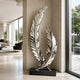 A mirror-polished stainless steel sculpture of two intersecting curved feathers on a black base. Displayed in a luxury hallway, this reflective metal art piece elevates modern indoor decor.