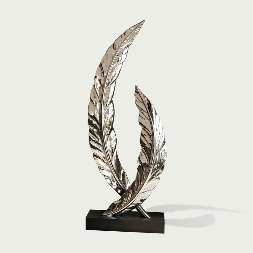 A mirror-polished stainless steel sculpture of two intersecting curved feathers on a black base on a white background