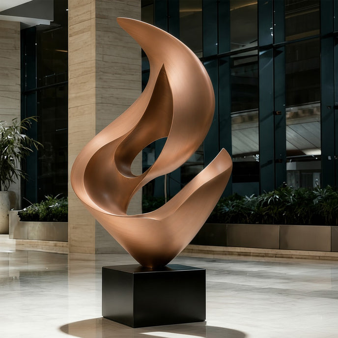 A mirror-polished stainless steel sculpture in a corporate lobby. The abstract design features overlapping fluid curves resembling a hollow sprout on a black base. This warm metallic art piece adds a luxurious atmosphere to the modern building entrance.