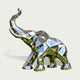 Three-quarter view of a contemporary low-poly stainless steel elephant sculpture featuring a raised trunk, broad geometric ears, and a strong four-legged stance. The entire elephant is formed from precisely defined triangular and polygonal surfaces, creating a distinctive faceted appearance. Its highly reflective mirror-polished silver finish captures blue sky and green landscape reflections across the angular metallic panels. Presented against a clean light background, the sculpture highlights its modern g