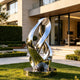 Large modern stainless steel loop sculpture showcasing a highly polished mirror finish and dynamic abstract design. The reflective metal artwork adds a luxurious contemporary touch to outdoor and commercial environments.