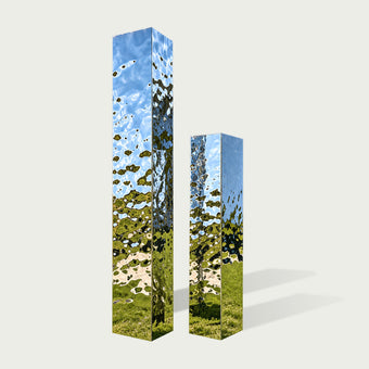 A modern stainless steel geometric column sculpture with mirror polished surfaces and angular twin structures. The reflective outdoor artwork creates dynamic light patterns in contemporary spaces.