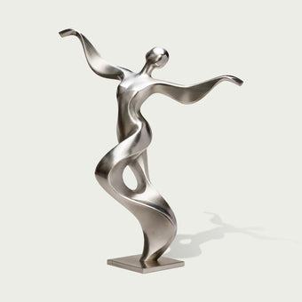 Full view of an abstract stainless steel dancer sculpture with a tilted rounded head, sweeping arms and a twisting ribbon-like torso forming an open loop, finished with brushed silver surfaces and polished accents on a square base against a light background.