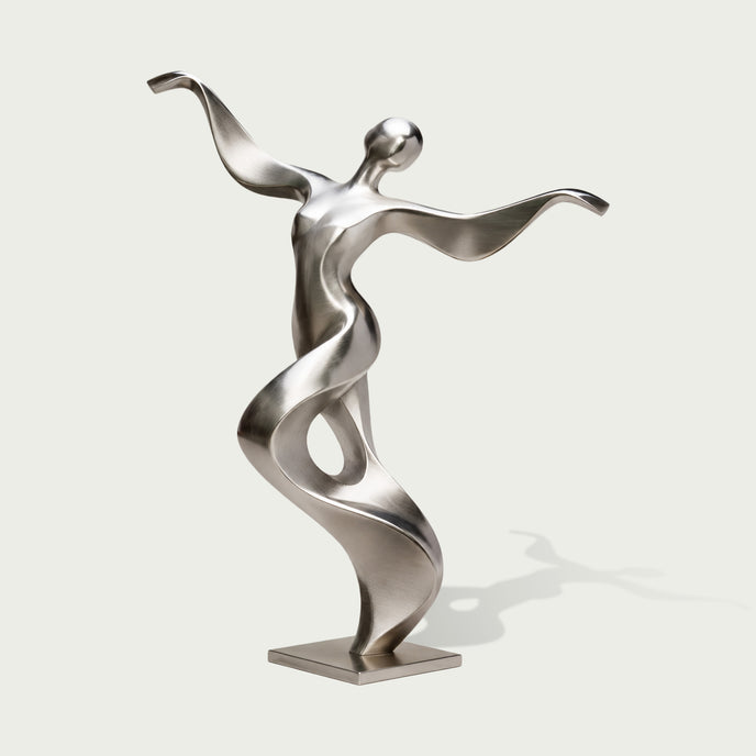 Full view of an abstract stainless steel dancer sculpture with a tilted rounded head, sweeping arms and a twisting ribbon-like torso forming an open loop, finished with brushed silver surfaces and polished accents on a square base against a light background.