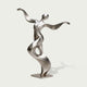 Full view of an abstract stainless steel dancer sculpture with a tilted rounded head, sweeping arms and a twisting ribbon-like torso forming an open loop, finished with brushed silver surfaces and polished accents on a square base against a light background.