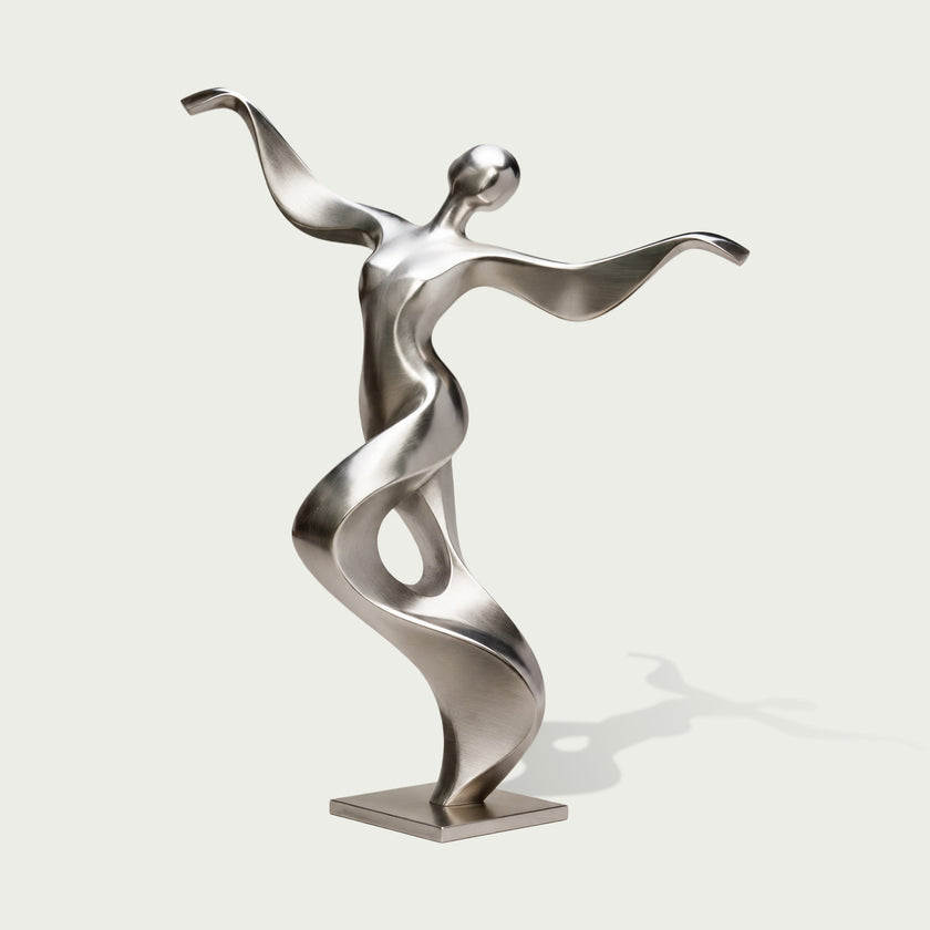 Full view of an abstract stainless steel dancer sculpture with a tilted rounded head, sweeping arms and a twisting ribbon-like torso forming an open loop, finished with brushed silver surfaces and polished accents on a square base against a light background.